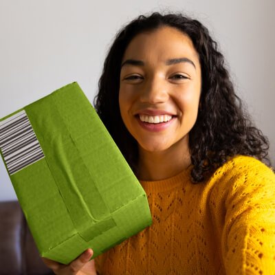 A young woman is holding up a green box with a barcode on it.