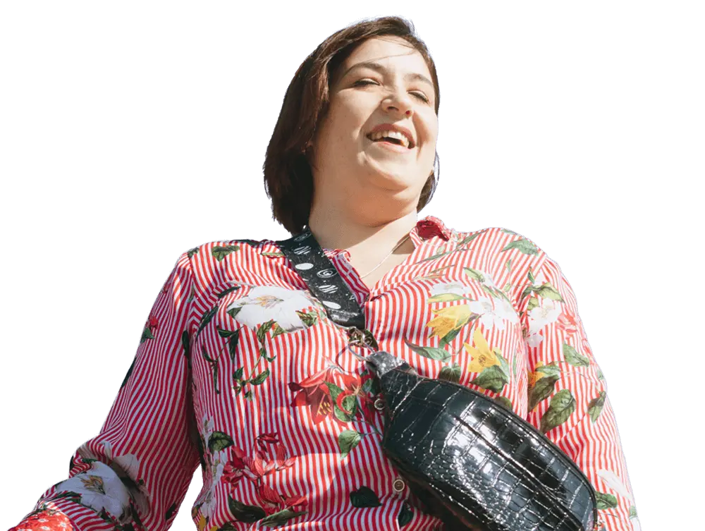 A person wearing a red and white striped floral shirt and a black crossbody bag is smiling and looking upwards.