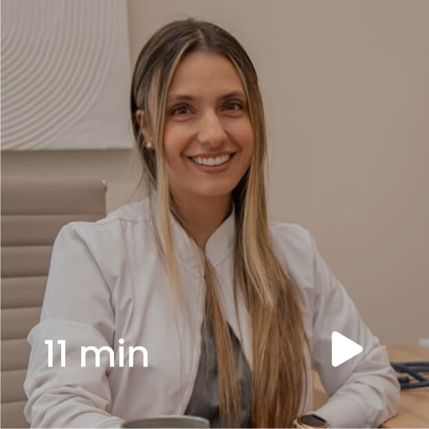 A woman with long hair sits at a table, smiling and wearing a white jacket. A play icon and "11 min" text is overlaid on the image.