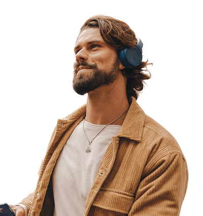 A man with a beard wearing a brown jacket, white shirt, and blue headphones looks upward, holding an object out of frame, against a plain white background.