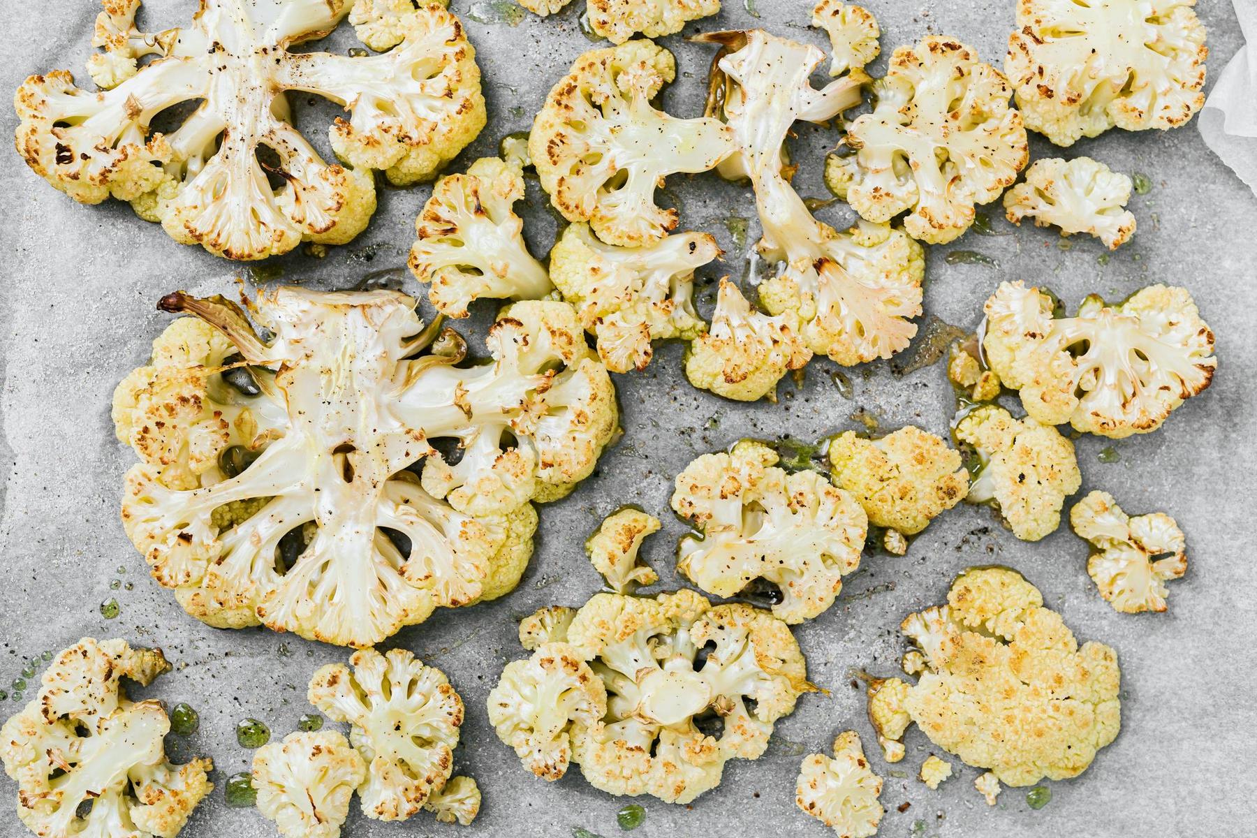 Slices of roasted cauliflower on parchment paper, lightly browned and seasoned with salt and pepper.