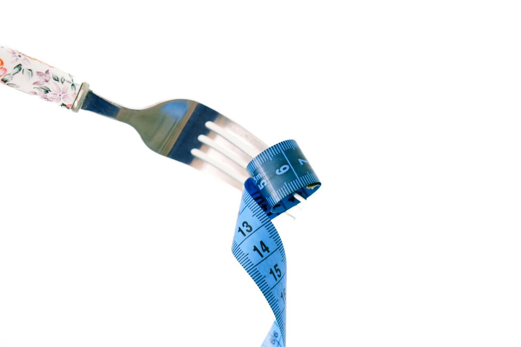 A fork holding a coiled blue measuring tape against a white background.