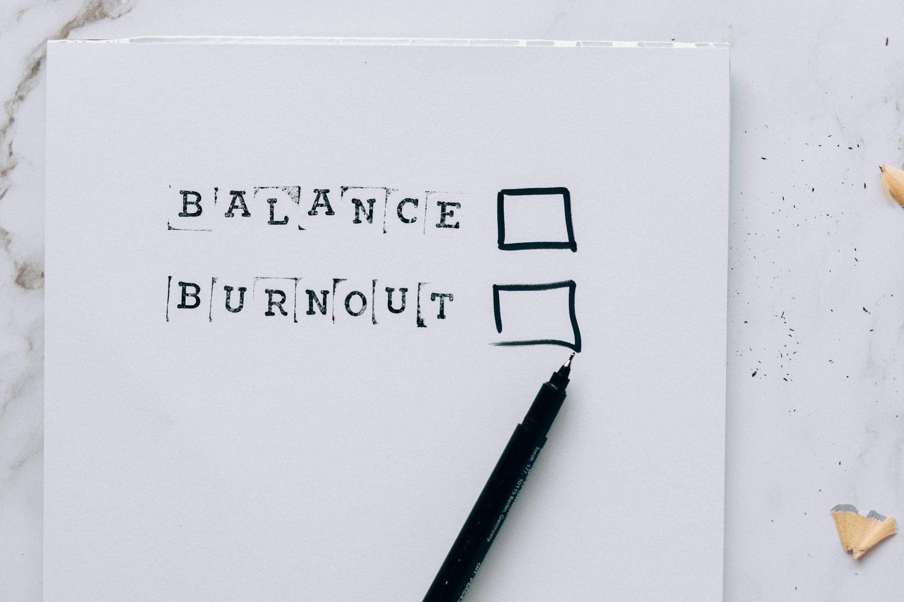 A paper with the words "Balance" and "Burnout" next to empty checkboxes, and a black marker lying below the text.