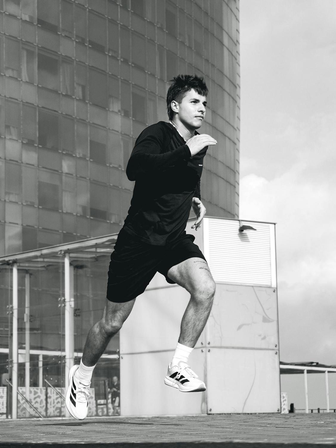 A man in athletic wear runs outdoors near a modern glass building.
