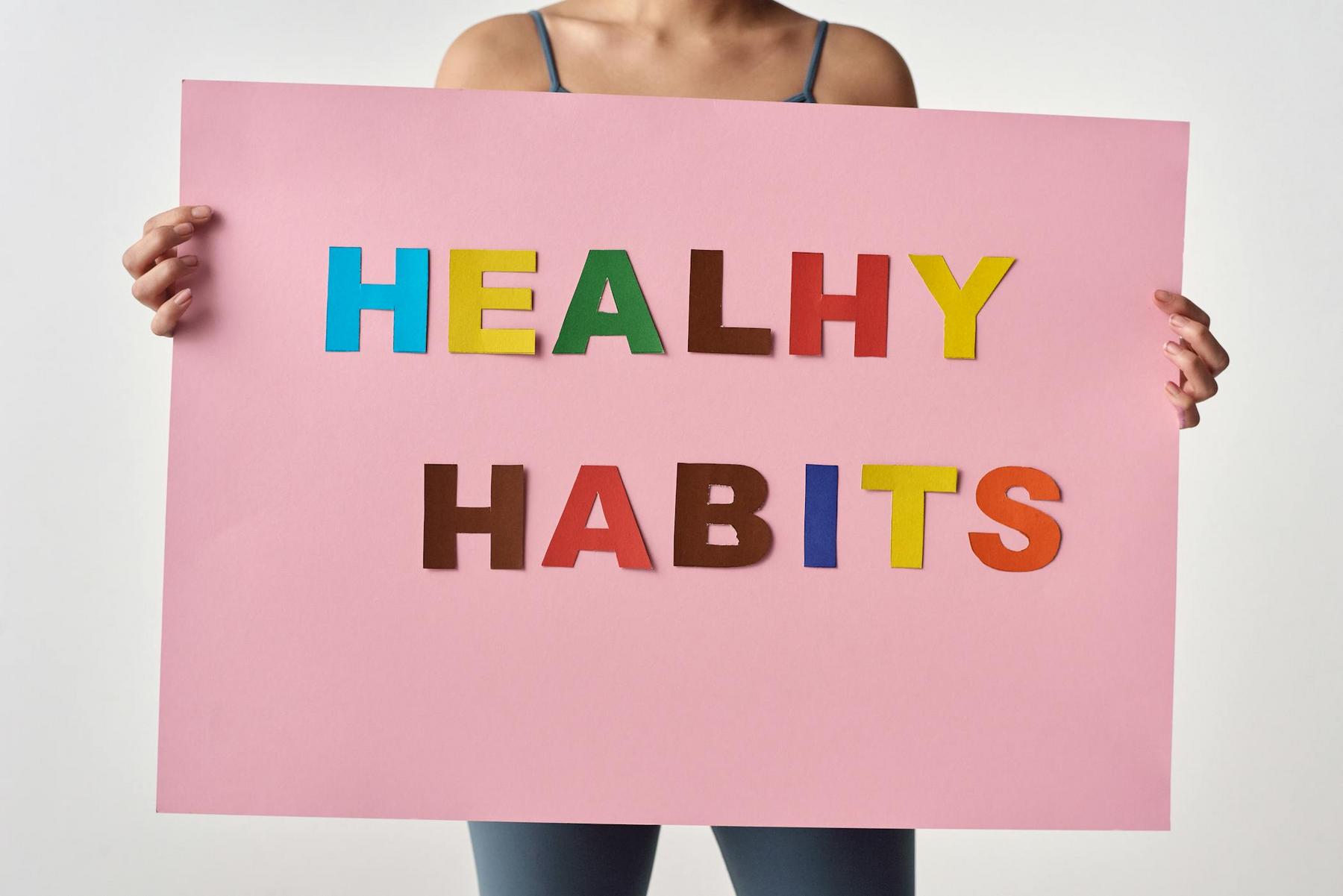 Person holding a pink sign with colorful letters spelling "HEALTHY HABITS.
