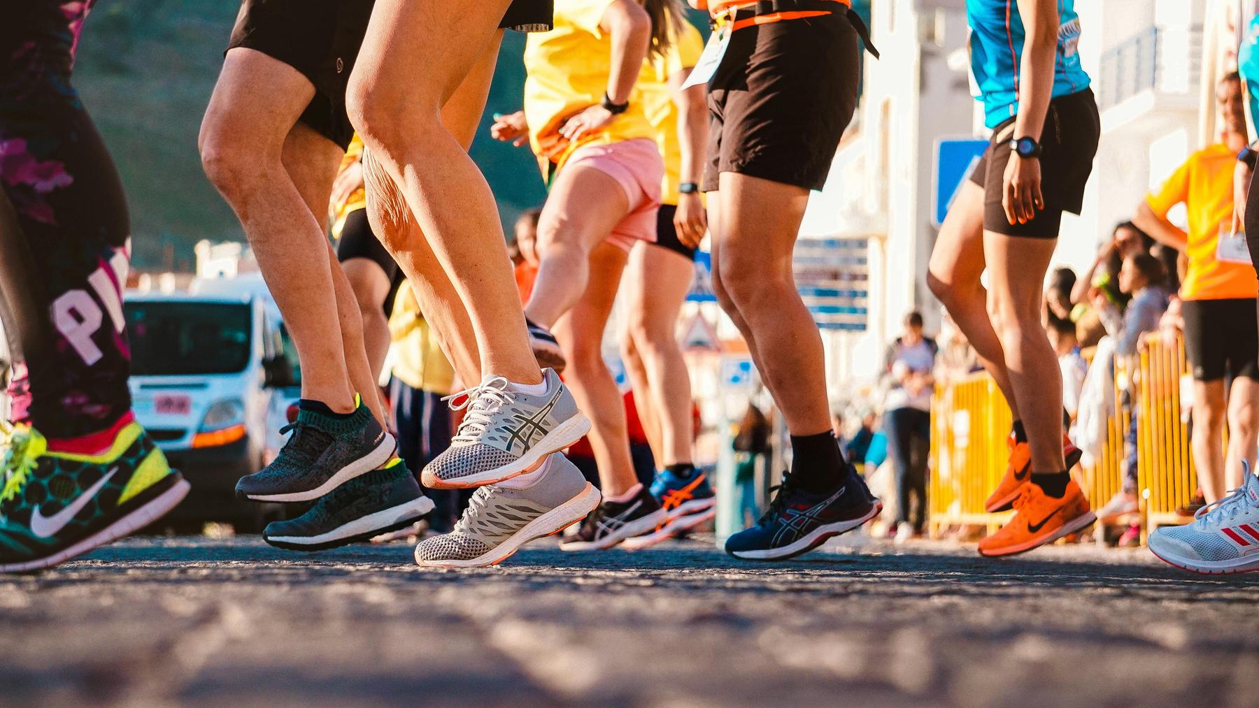 A group of runners in athletic clothing and sneakers participates in a race or event on a paved street.