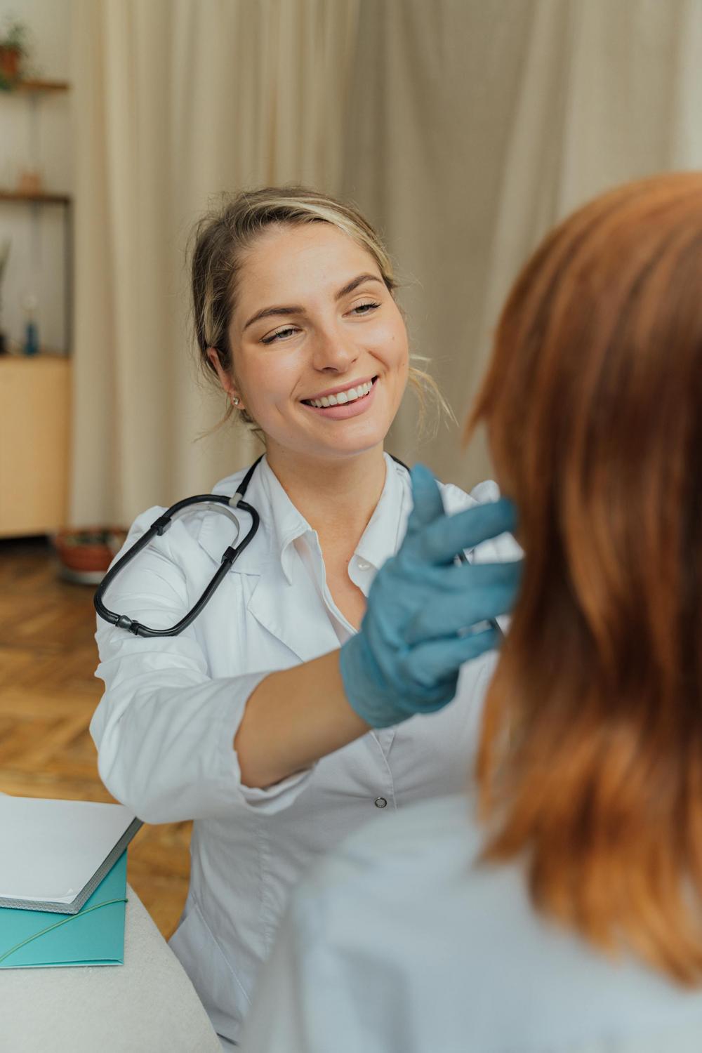 A doctor wearing a stethoscope and blue gloves examines a patient with red hair in a medical office setting.