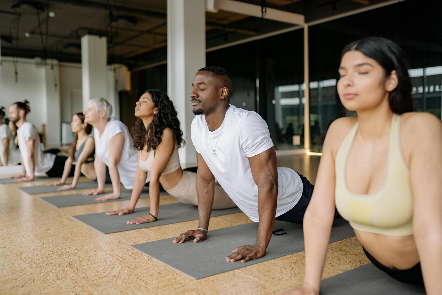 A group of people in athletic wear practice yoga together indoors, performing the upward-facing dog pose on yoga mats.