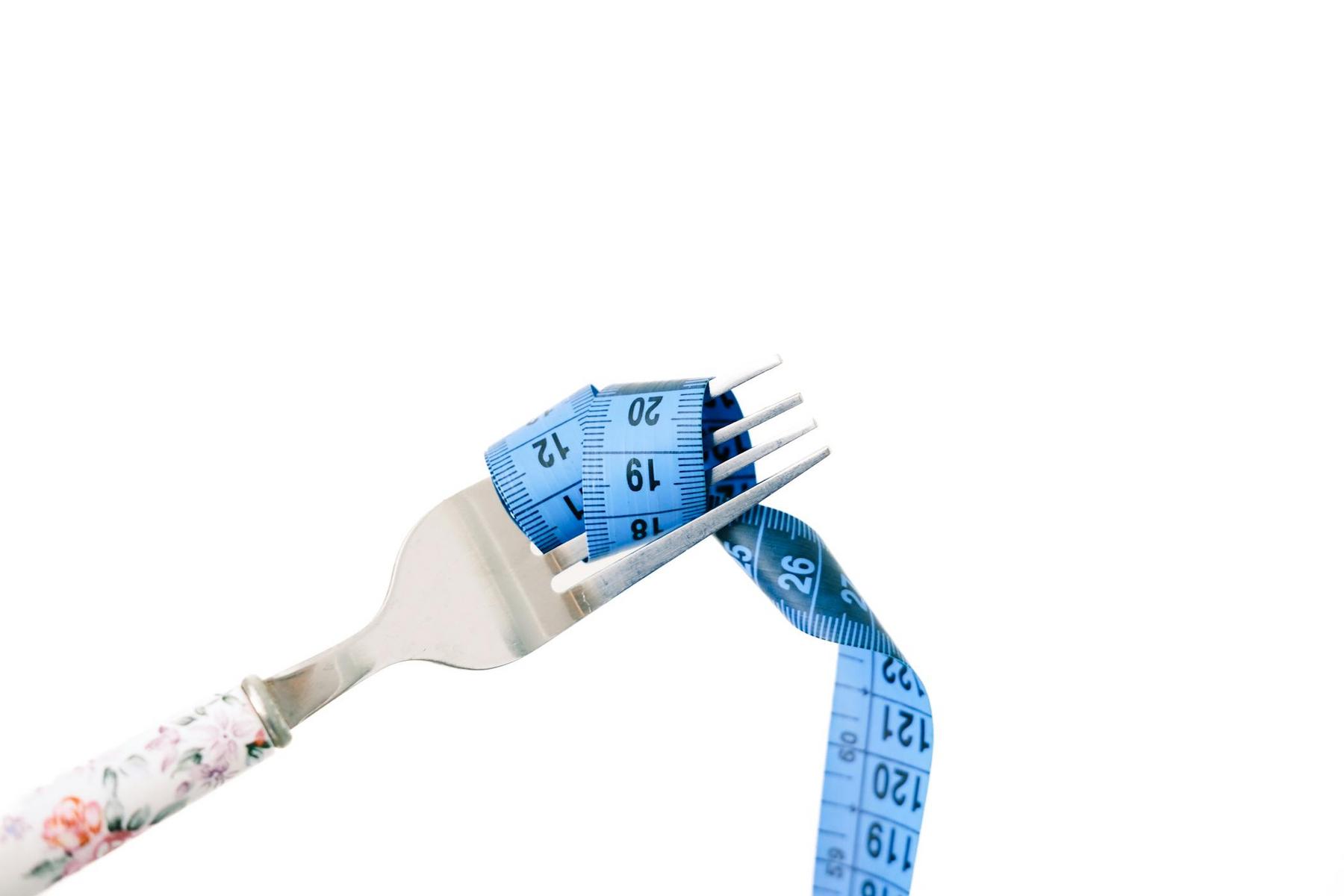 A fork with a floral handle holds a coiled blue measuring tape against a white background.
