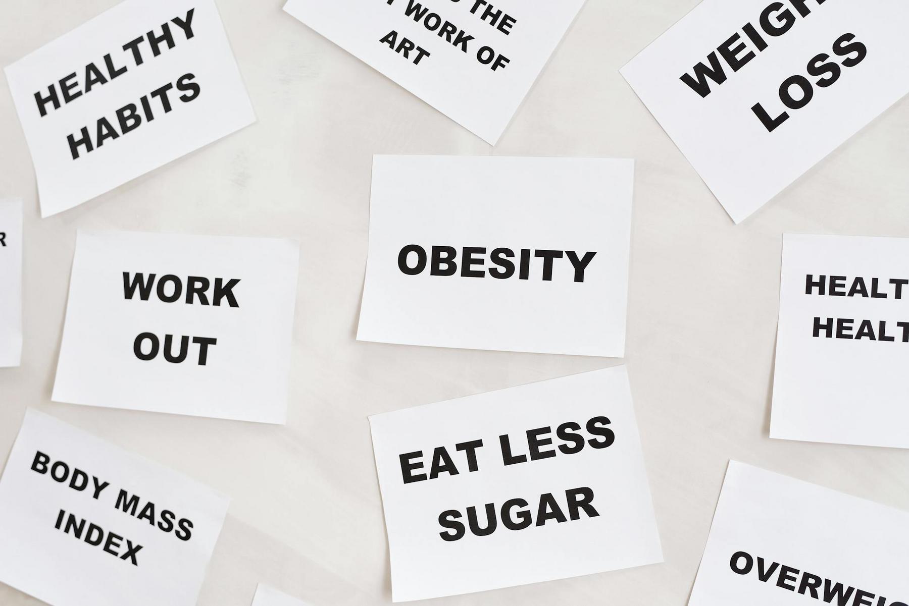Scattered white cards with words like "Obesity," "Eat Less Sugar," "Work Out," and "Weight Loss.