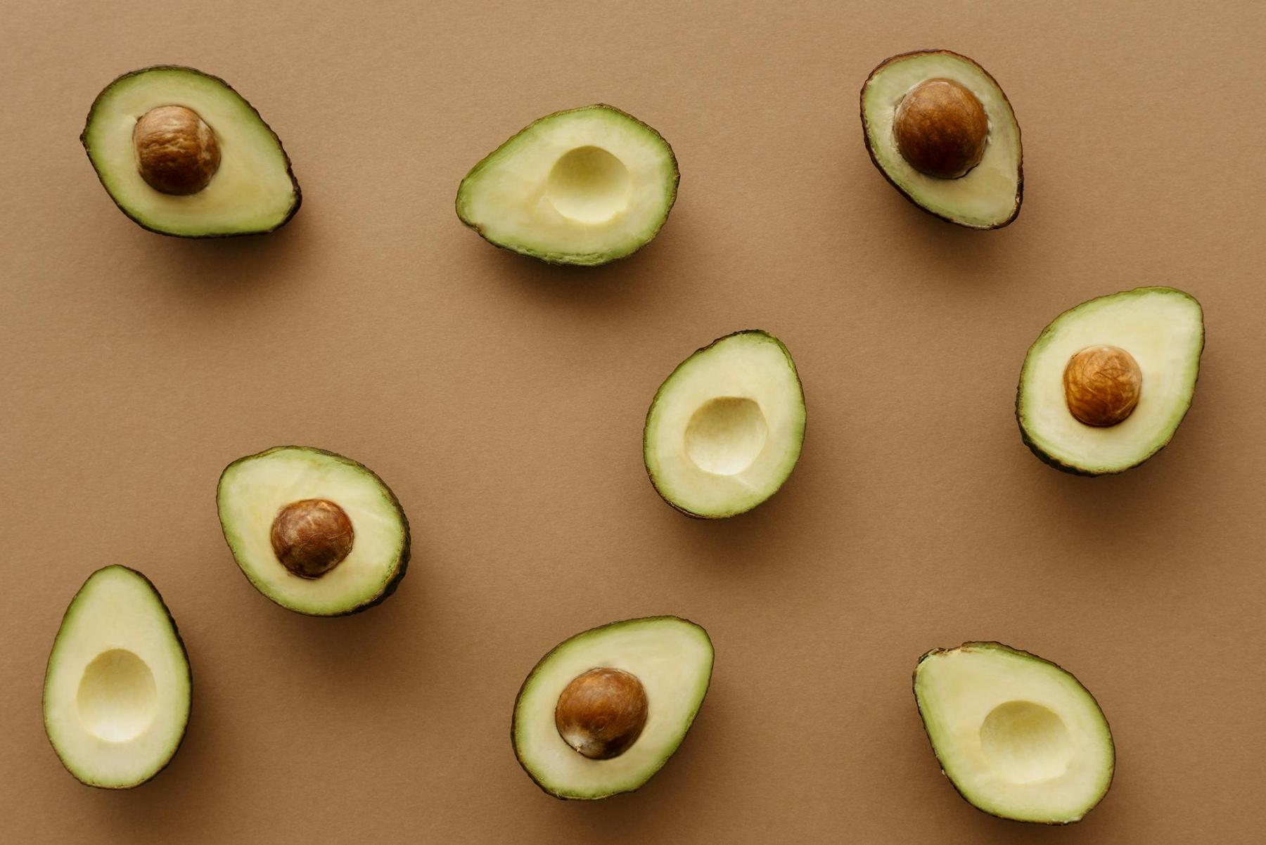 Halved avocados with and without pits arranged on a brown surface.