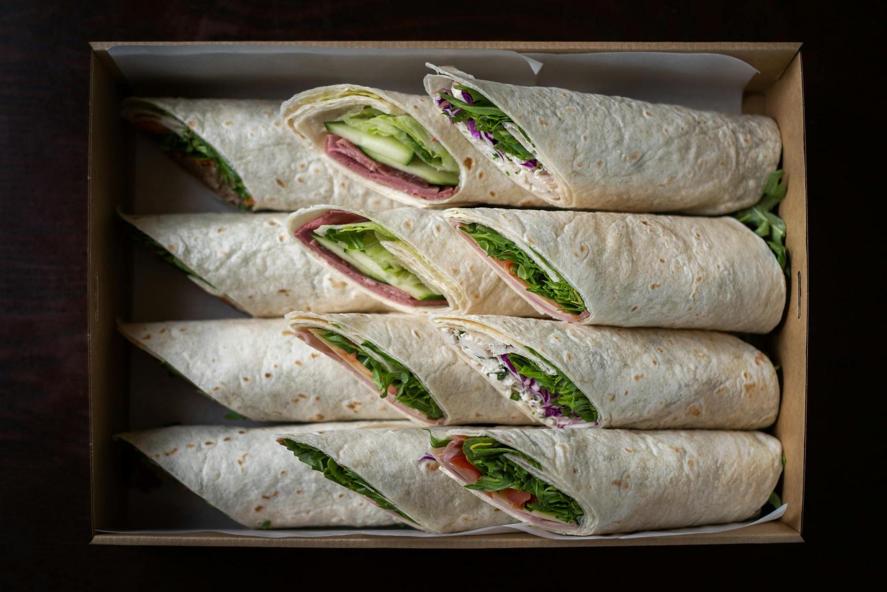 A box containing six tortilla wraps filled with various vegetables and deli meats, arranged neatly in two rows.