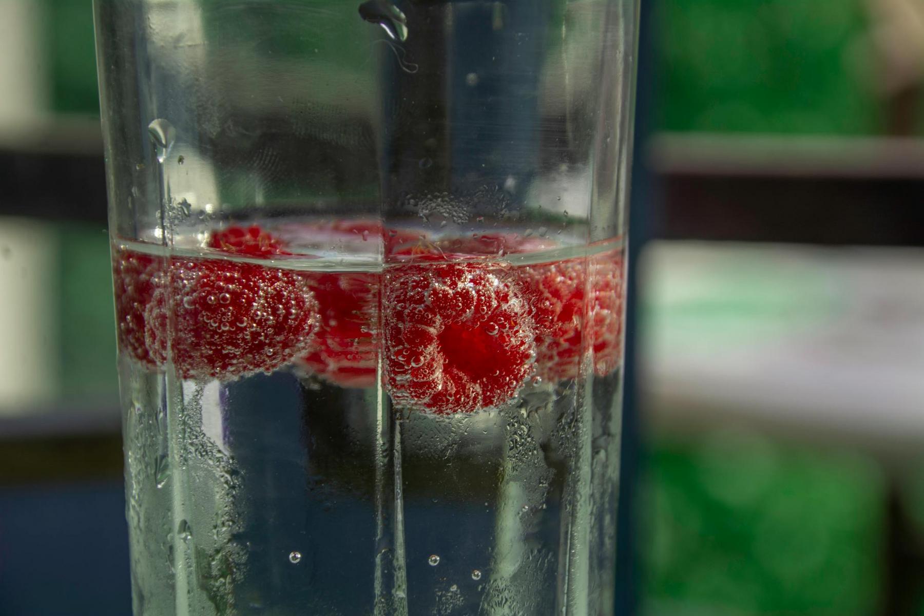Close-up of raspberries in a glass of sparkling water, with bubbles clinging to the fruit.