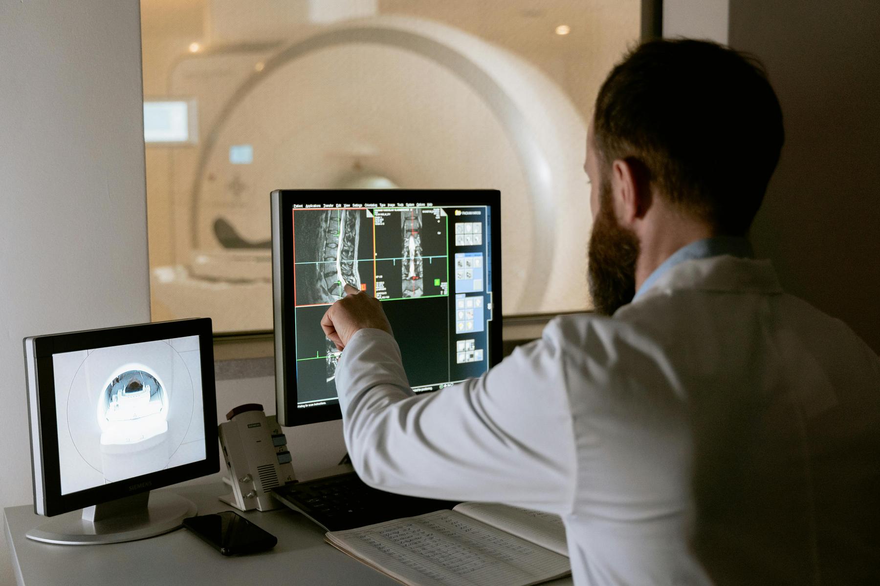A doctor reviews and analyzes MRI scan images on computer screens in a medical imaging room.