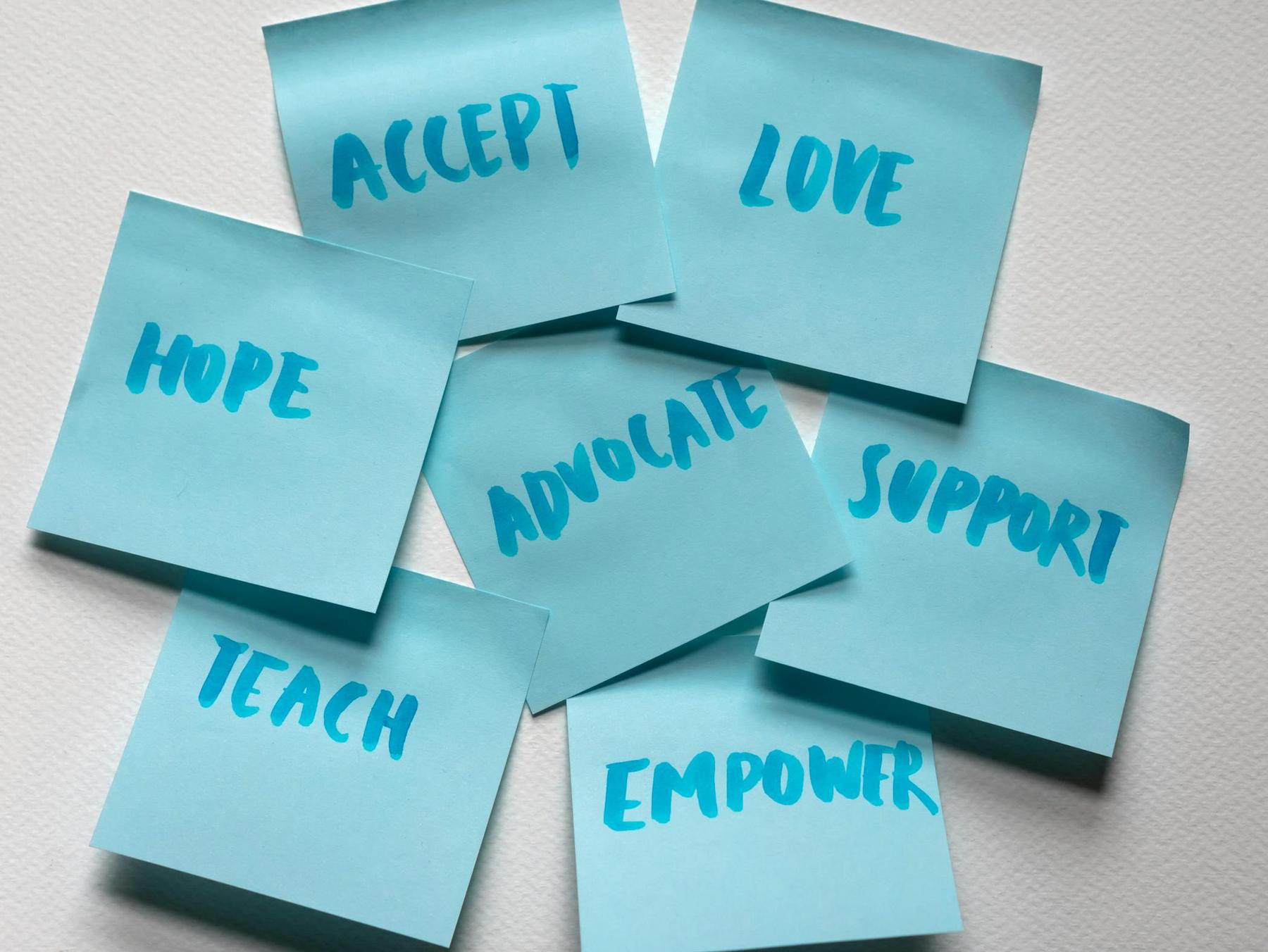 Seven blue sticky notes are arranged on a white surface, each displaying a word: accept, love, hope, advocate, support, teach, and empower.