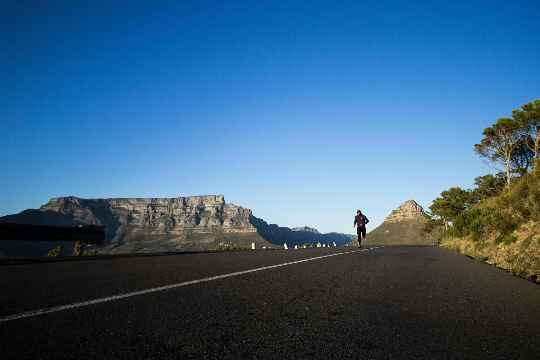 A person runs on an empty road with mountains and clear blue sky in the background.