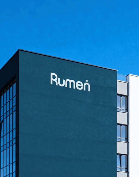 A modern building with the word "Rumen" displayed on its dark blue facade, set against a clear blue sky.