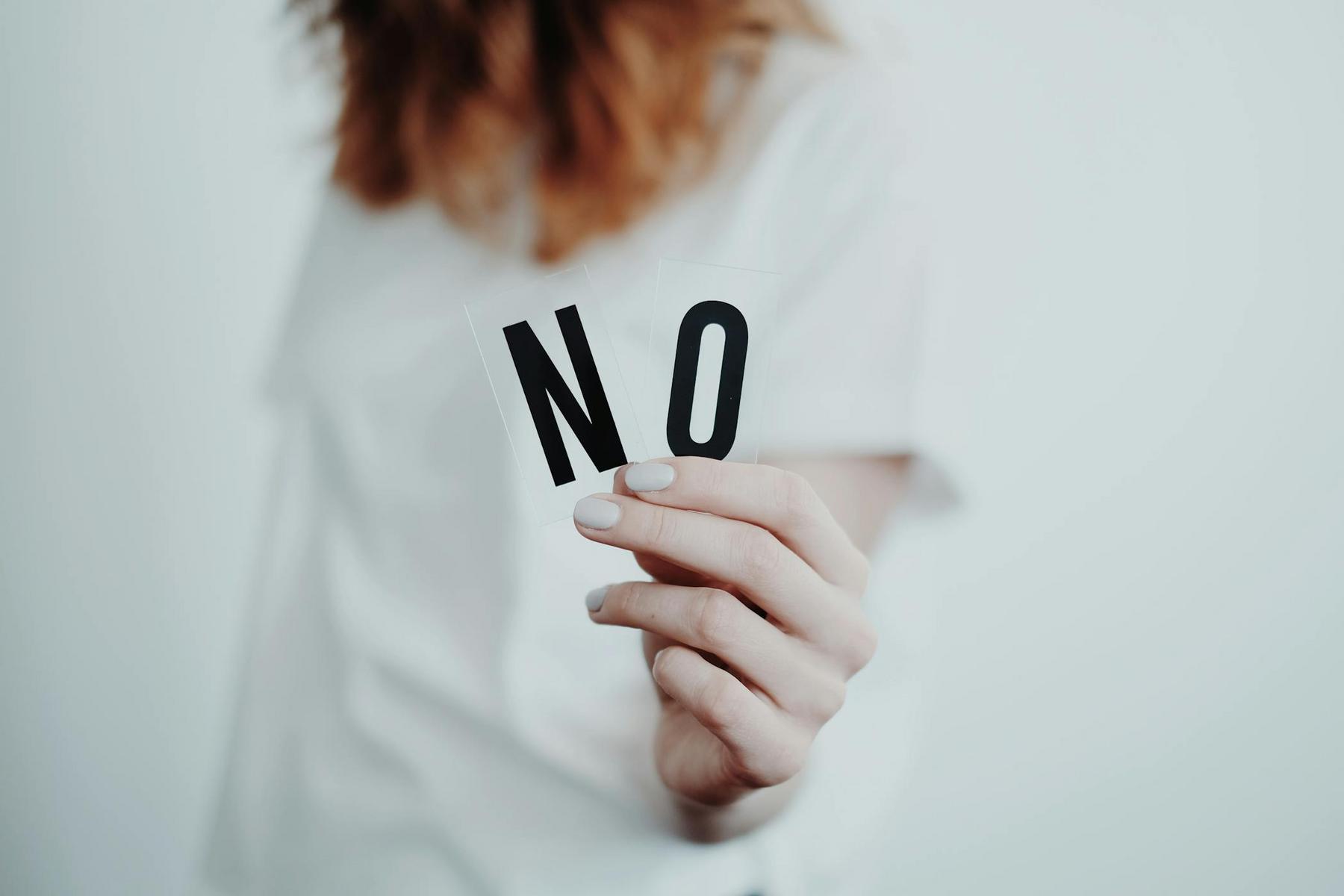 A person holds up two cards with the letters "N" and "O," spelling "NO," against a plain background.