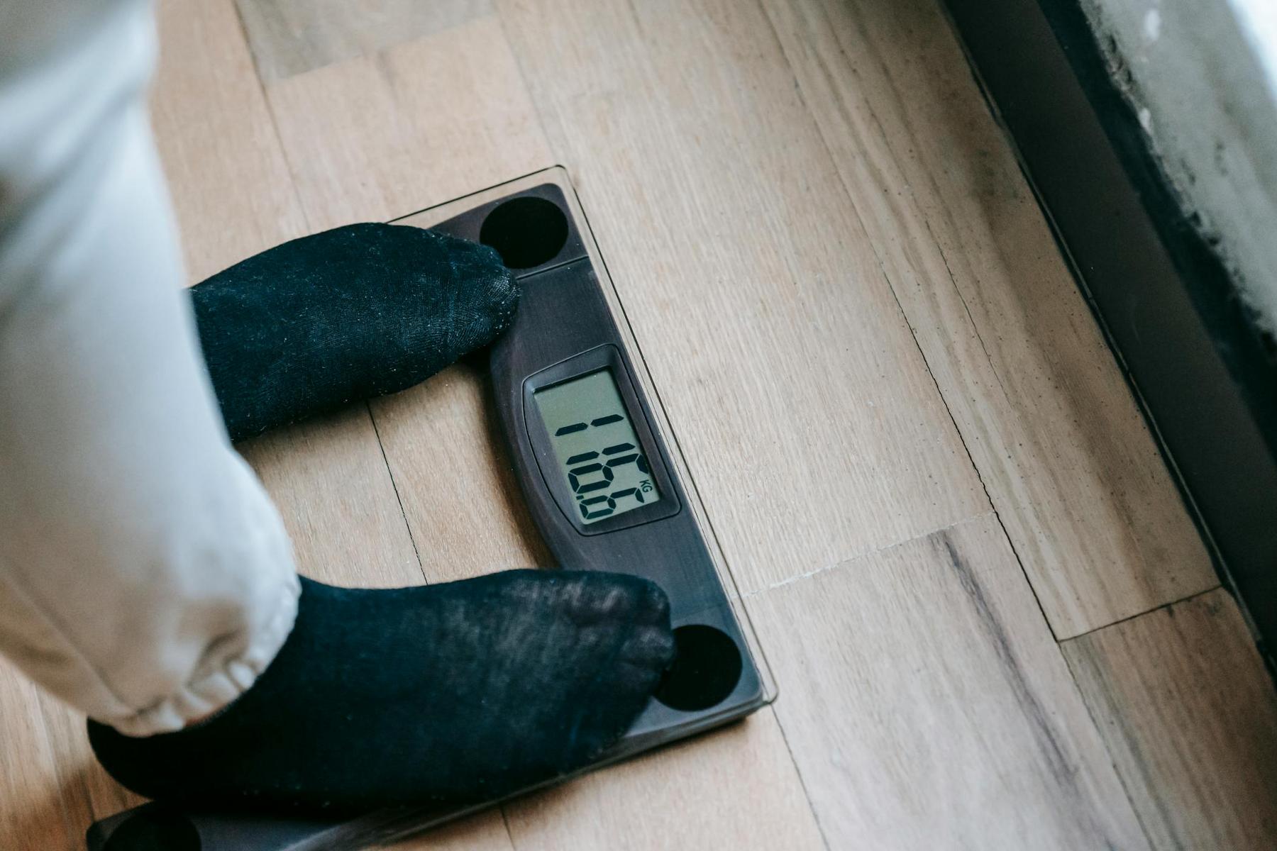 Person wearing black socks standing on a digital scale displaying a weight of 106.4 pounds on a wooden floor.