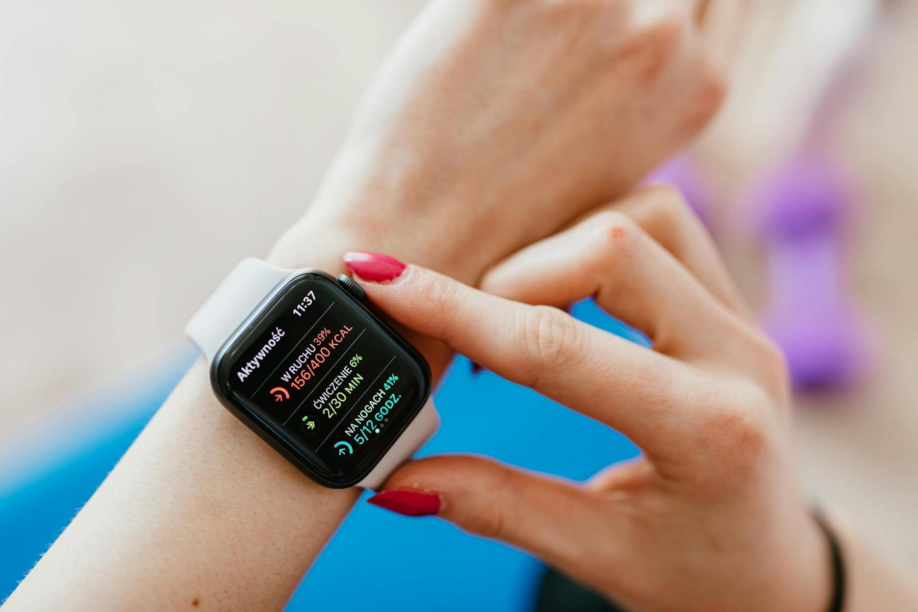 A person wearing a smartwatch with a fitness tracking display is tapping the screen with their finger.