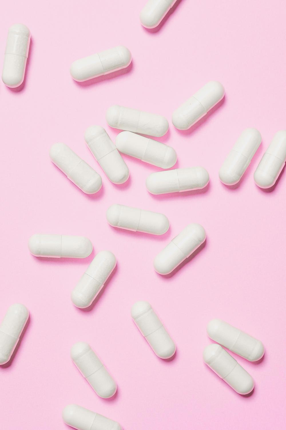 White capsules scattered on a pink background.