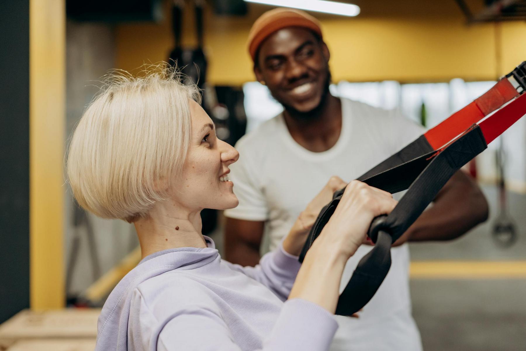 Woman exercising with suspension straps in a gym, guided by a trainer.