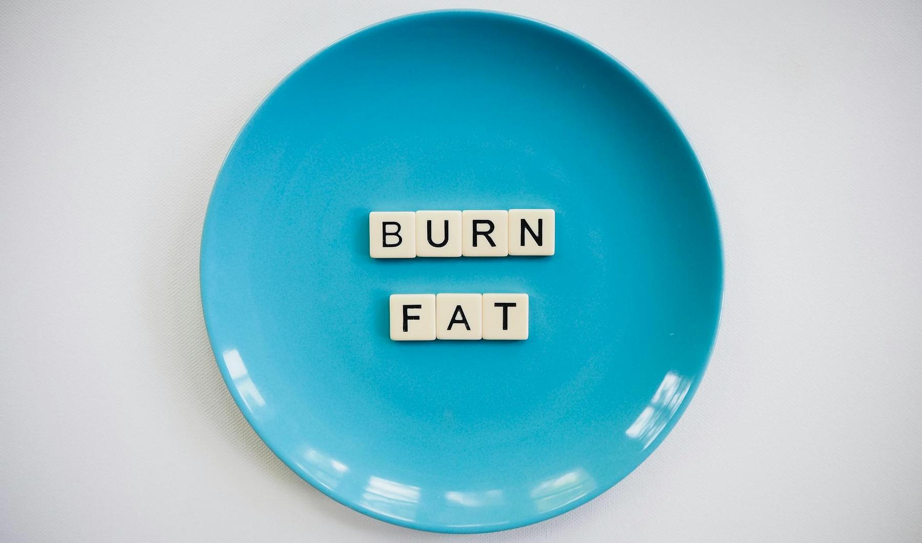 Blue plate with Scrabble tiles spelling "BURN FAT" in the center, against a plain background.